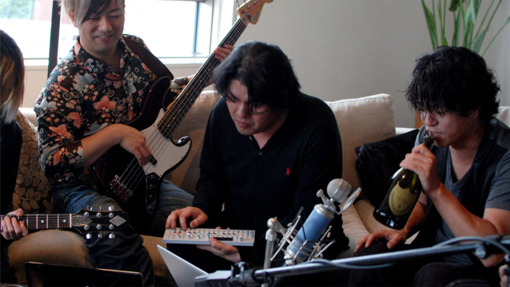 كينجي إينو يتوسط رفاقه أثناء إحدى جلسات العزف (ننصحك بالاستمتاع إلى موسيقى إينو أثناء قراءة المقال)